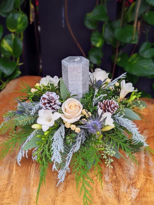 A round centrepirce with a silver pillar candle surrounded by winter greenery, white freesia, thistle and silver cedar.