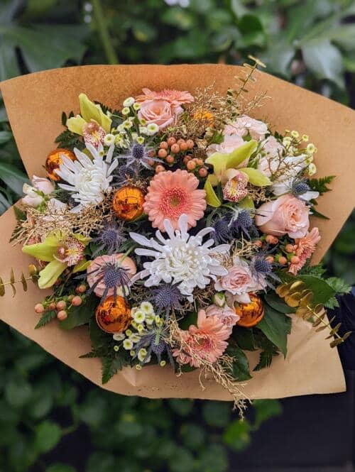 a gardeney winter bouquet featuring peach roses, thistle, white mums, green orchids, bronze ornaments and so much more.