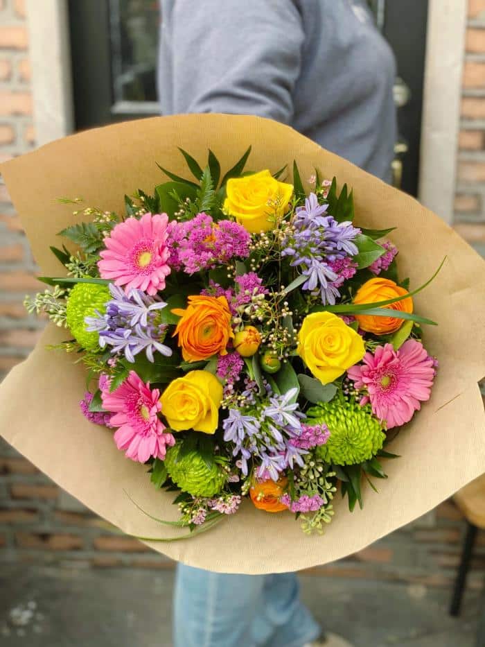 The Watering Can | A large rainbow coloured hand tied bouquet wrapped in brown paper.