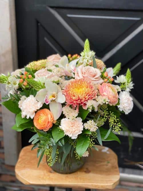 The Watering Can | A large blush and orange coloured bouquet in a blue ribbed glass vase.