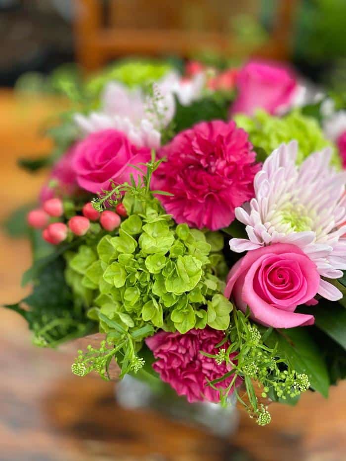 The Watering Can | Bright pink roses, carnations and hypericum, with blush mums and green hydrangea in a compact bouquet.