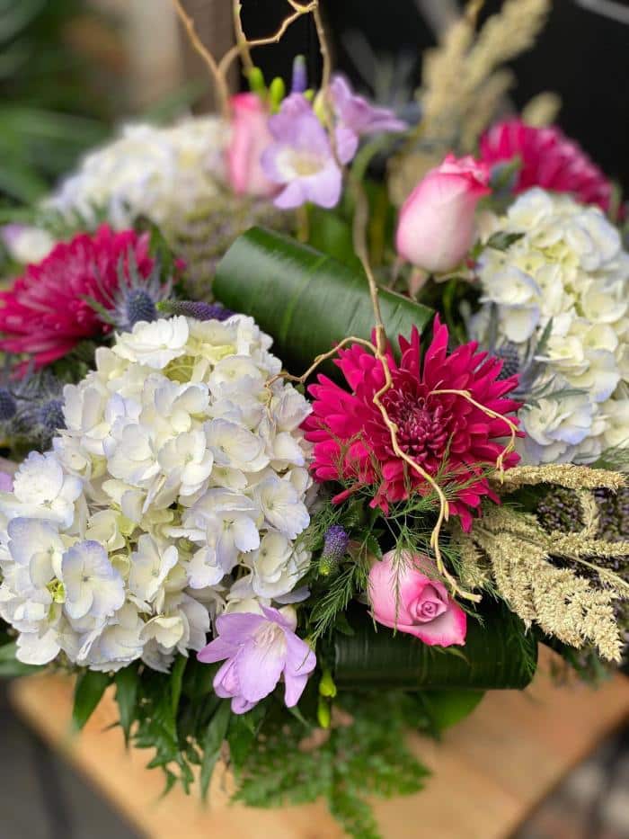 The Watering Can | Close up of a pale bluw hydrangea, plum mum pink rose in a large handtied bouquet.