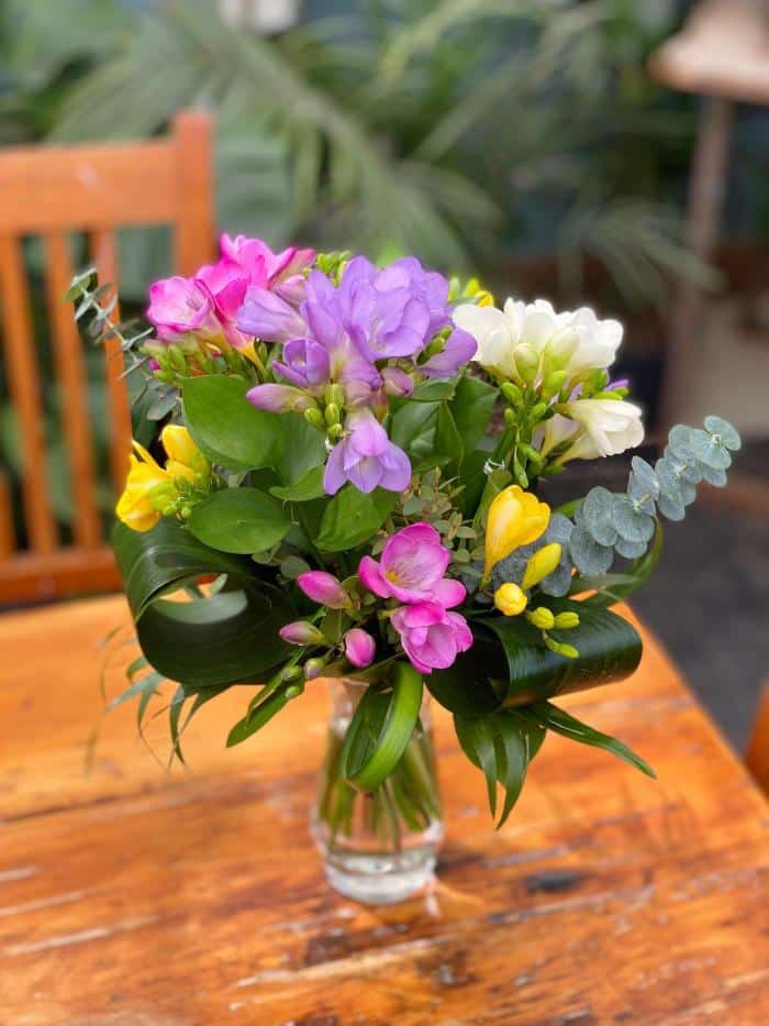 A bouquet and vase overflowing with freesia in purple, white, pink and yellow