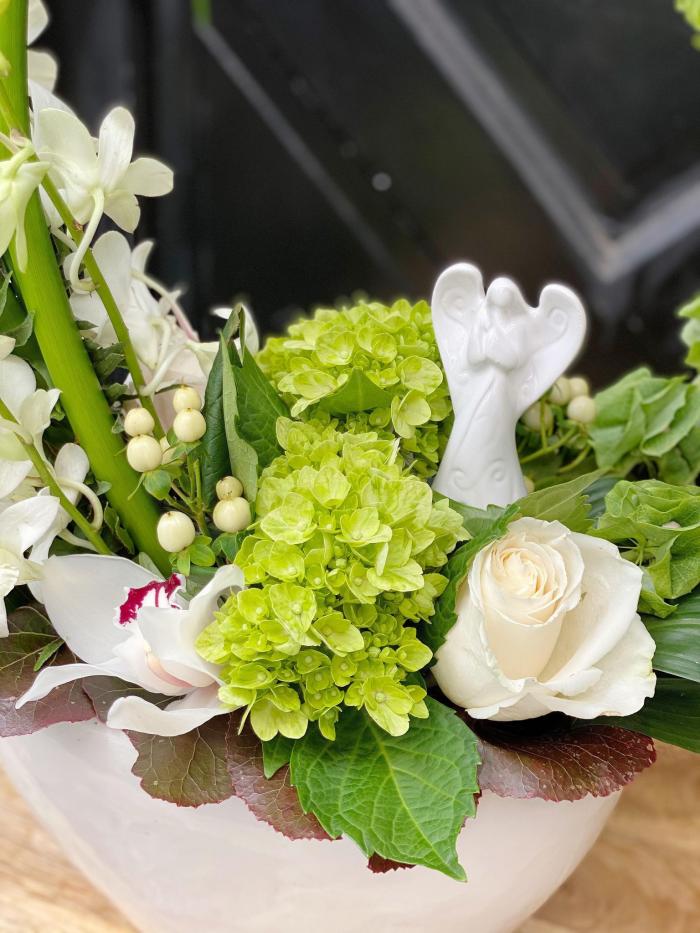 The Watering Can | Close up of the angel satuette and flowers around it. Pictured are green hydrangea, white cymbidium orchids, and white roses.