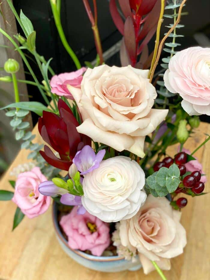 The Watering Can | Photograph looking down at the blush roses, white ranunculus, lavender, and burgundy blooms in a european arrnagement.