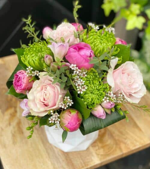 The Watering Can | A green and pink bouquet featuring peonies in a white faceted ceramic vase.