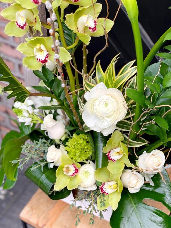 The Watering Can | Close up of a large Euopean style floral arrangement. White ranunculus, green cymbidium orchids, white roses and tropical greens can be seen.