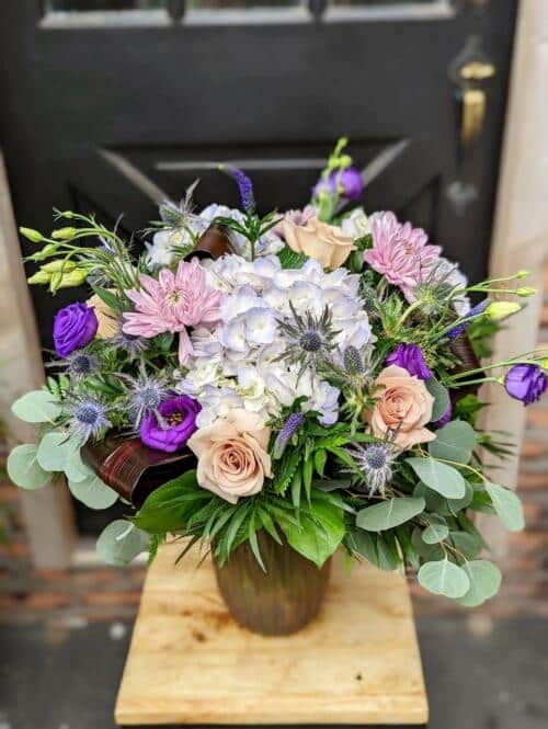 The Watering Can | A large bouquet in a ribbed purple glass vase of a variety of mauve, purple, and lavender blooms.