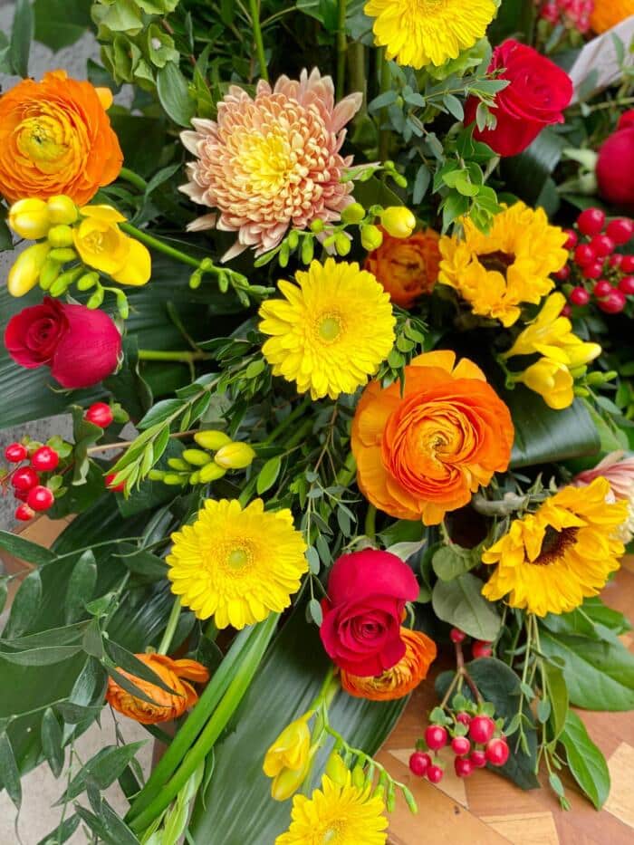 The Watering Can | Orange rununculus, yellow gerbera daisies, and mums in a large floral display.