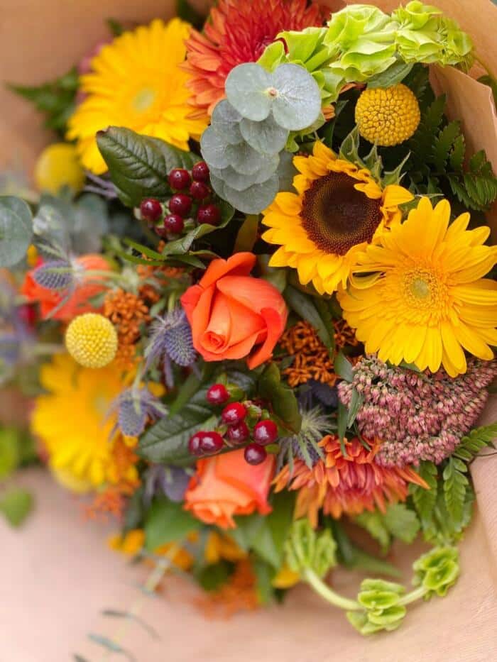 The Watering Can | Close up of the warm toned orange and yellow blossoms in a large hand-tied bouquet.