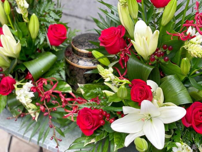 The Watering Can | Close up of the red roses, white lilies, and annabelle orchids in a cermation display.