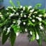 The Watering Can | An all white casket spray made with calla lilies, bells of Ireland, white roses, dendrobium orchids, freesia in a bed of lush greenery.