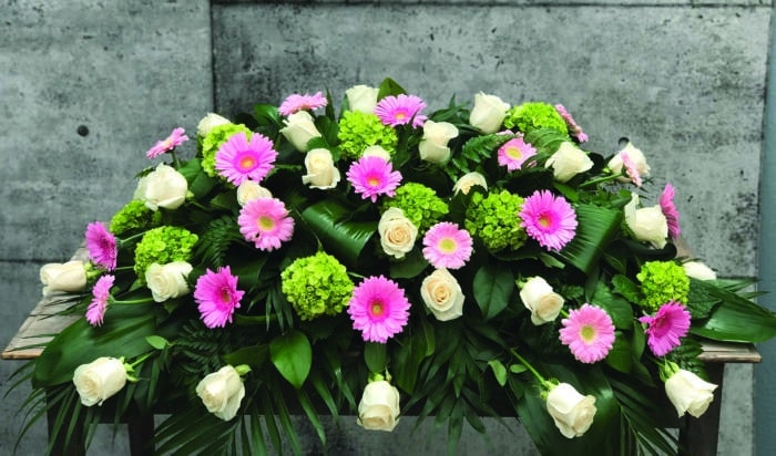 The Watering Can | A casket spray made with white roses, green hydrangea, and pink and white gerbera daisies in a lush bed of greens.