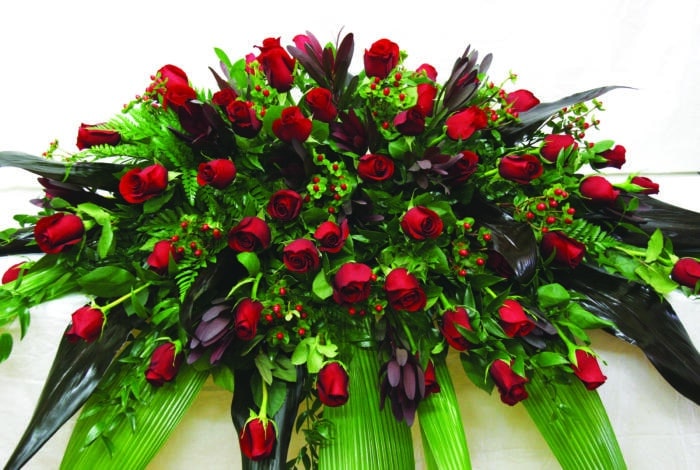 The Watering Can | An all red casket spray with roses, leucadendron, and hypericum flowers in a lush bed of greens.