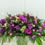 The Watering Can | A purple casket spray made with white calla lilies, purple roses, lavender mums, green hydrangea, dark purple stock, soft pink spray roses, stars of Bethlehem, purple freesia, purple veronica, hot pink gerberas, purple tulips, and white hypericum on a bed of greens.