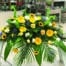 The Watering Can | A casket spray made with purple agapanthus, bells of Ireland, sunflowers, yellow gerberas, soft yellow roses, and white roses on a bed of greens.