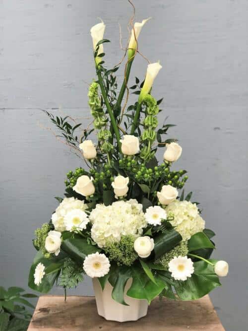 The Watering Can | An all white side spray made with calla lilies, bells of Ireland, roses, hypericum, hydrangea, trachelium, gerberas, rununculus, curly willow and a variety of greens.