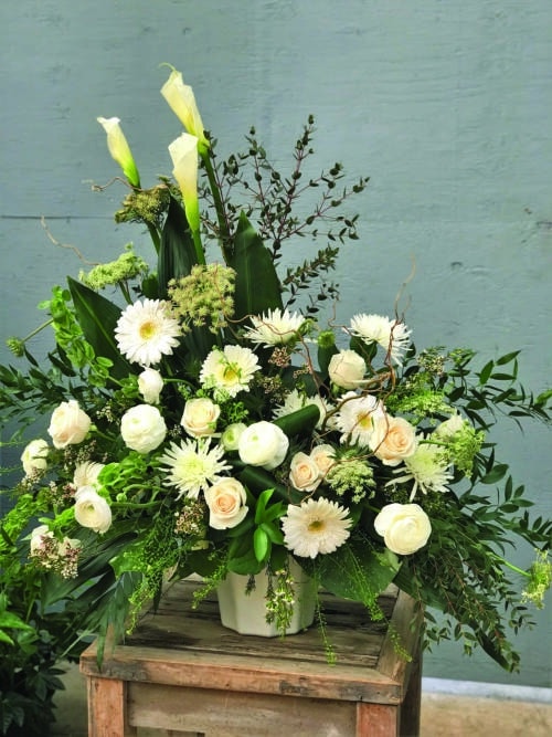 The Watering Can | An asymetrical white side spray with calla lilies, gerberas, roses, mums, rununculus, bells of Ireland, queen Anne's lace, waxflower, curly willow, and a mix of greens.