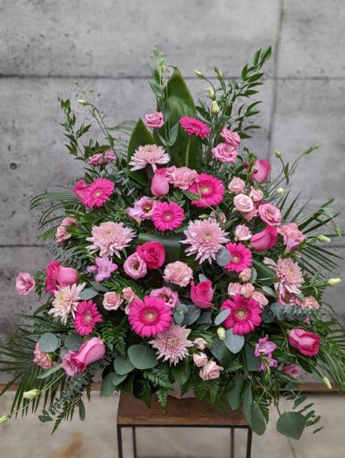 The Watering Can | A large pink side spray made with gerberas, lisianthus, mums, roses, carnations, freesias, eucalyptus, and greens.