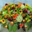 The Watering Can | A round casket spray made with antique hydrangea, orange roses, bells of Ireland, sunflowers, peach hypericum, bronze mums, pink sedum, yellow freesia, burgundy dahlias, orange gerberas, and thin grapevine pieces with a variety of greens.