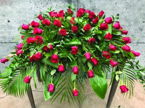 The Watering Can | A casket spray made with red roses and a variety of lush greens.