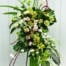 The Watering Can | A stunning modern easel spray made with white calla lilies, bells of Ireland, white & green rununculus, white helleborus, green cymbidium orchids, white dendrobium ochids, light pink roses, fantail willow, and tropical greens.