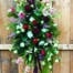 The Watering Can | An easel spray made with burgundy leucadendron, soft pink astilbe, burgundy dahlias, red roses, white mums, peach stock, peach hypericum, cream lisianthus, soft pink waxflower, white freesia on a bed of greens.