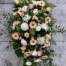 The Watering Can | A peach and white easel spray made with roses, mums, rununculus, hypericum, statice, and gerberas on a lush bed of greens.