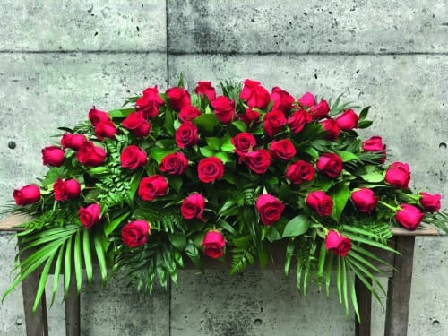The Watering Can | A casket spray made with red roses amid a bed of greenery.