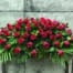 The Watering Can | A casket spray made with red roses amid a bed of greenery.