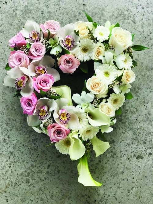 The Watering Can | A 12" open heart so full of flowers, it almost appears to be soild. soft pink roses, white roses, white calla lilies, white cymbidium orchid blooms, white dendrobium orchids, white waxflower, and white gerberas rest amongst Italian ruscus.