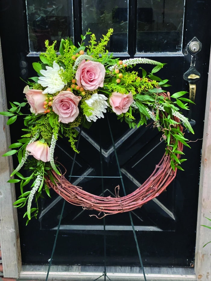 The Watering Can | A grapevine wreath with a spray of flowers at the top left.