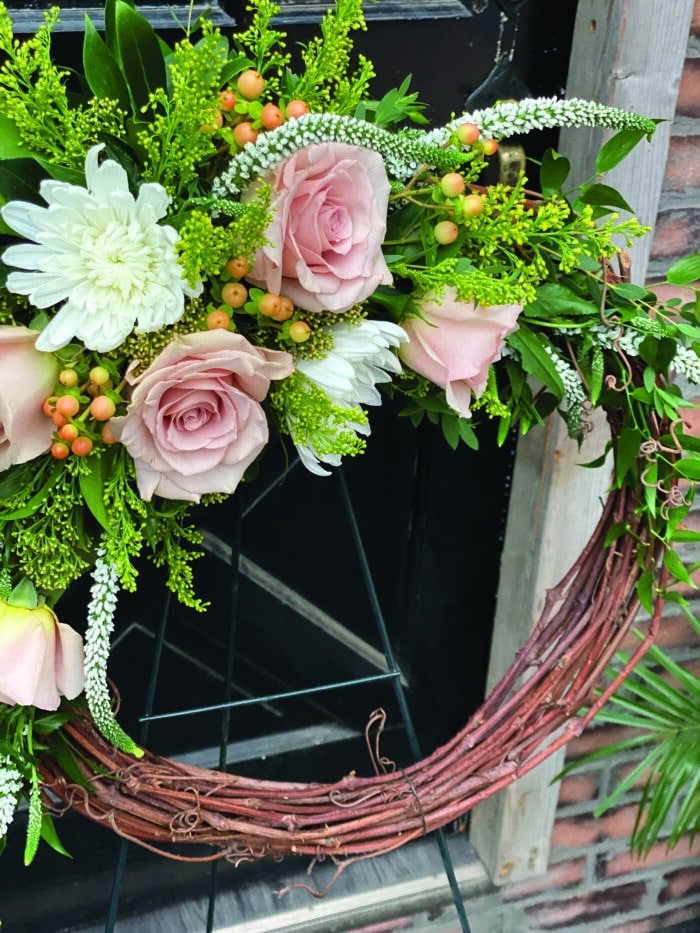 The Watering Can | Blush roses, white mums, peach hypericum, white veronica, solidago, and ruscus on a grapevine wreath.