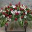 The Watering Can | A red and white casket spray made with red roses, white mums, white trachelium, white mini gerbera daisies, and white dendrobium orchids in a bed of lush greens.