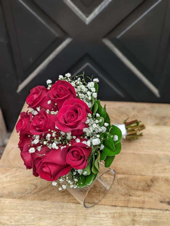 The Watering Can | A red rose bouquet with baby's breath and minimal green wrapped in stain laying on a table.