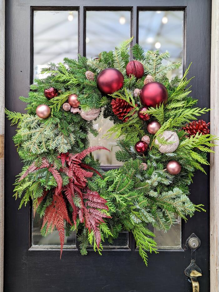 The Watering Can | A wreath with asymetrical burgundy and rose balls, pine cones balanced by a burgundy fern.