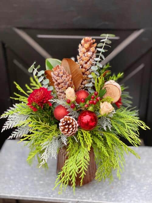 The Watering Can | A red and natural bouquet made with winter greens and pinecones in a brown ribbed glasss vase.