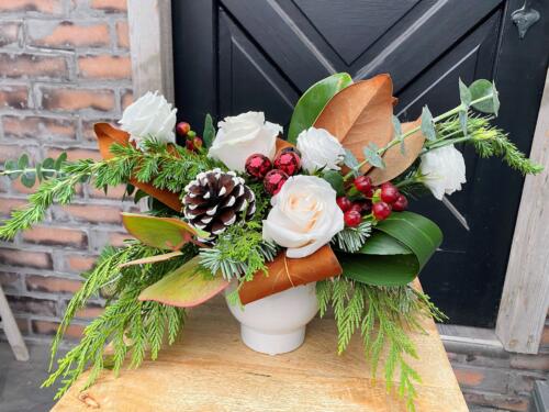 The Watering Can | A red and white European style arrangement with winter greens and pine cones in a white container.
