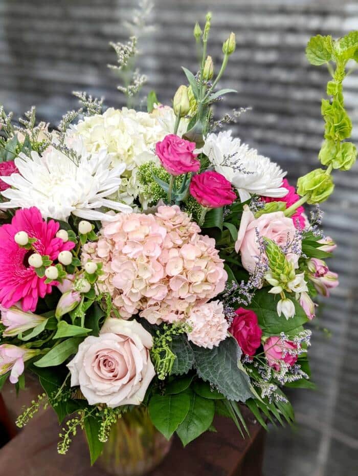 The Watering Can | Alternate view of a large pink and white bouquet with garden greens in a pink glass vase.