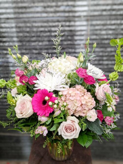 The Watering Can | A large pink and white bouquet with garden greens in a pink glass vase.