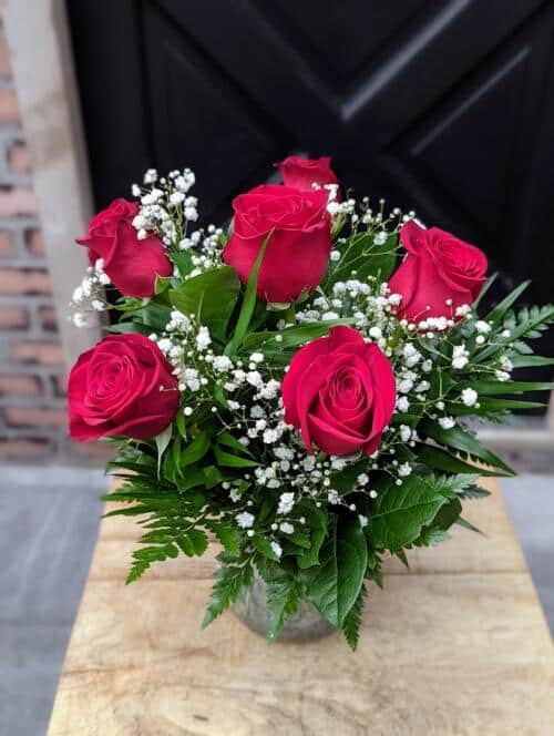 an iridescent vase with 1/2 dozen red roses, greenery and babys breath