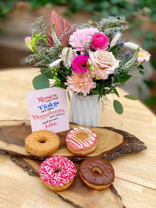 The Watering Can | A pink bouquet in a white vase with a card and 4 doughnuts.