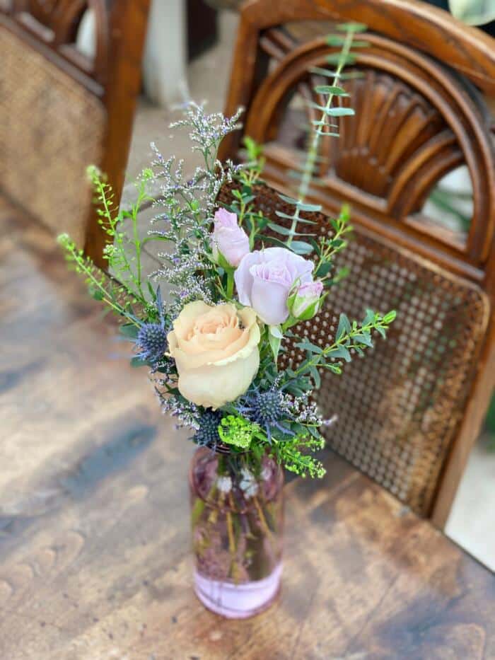The Watering Can | A small bouquet of roses and garden greens in a lavender glass vase.