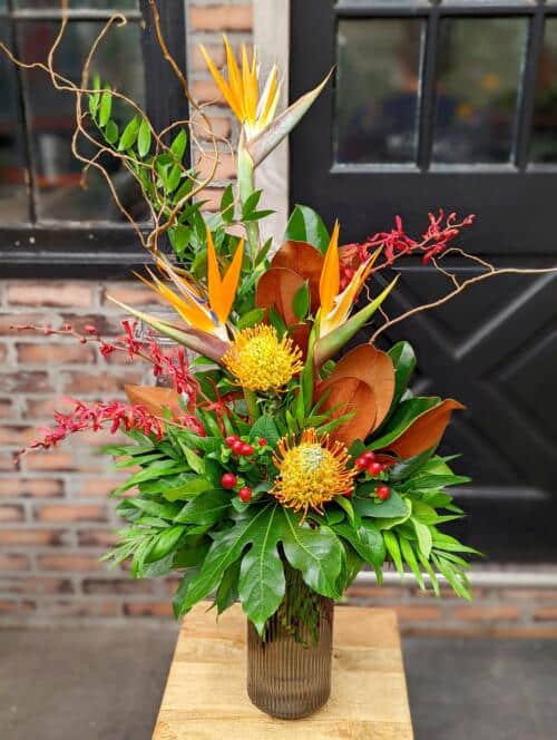 The Watering Can | A bright and tropical bouquet with birds or paradise and pincushion in a brown glass vase.
