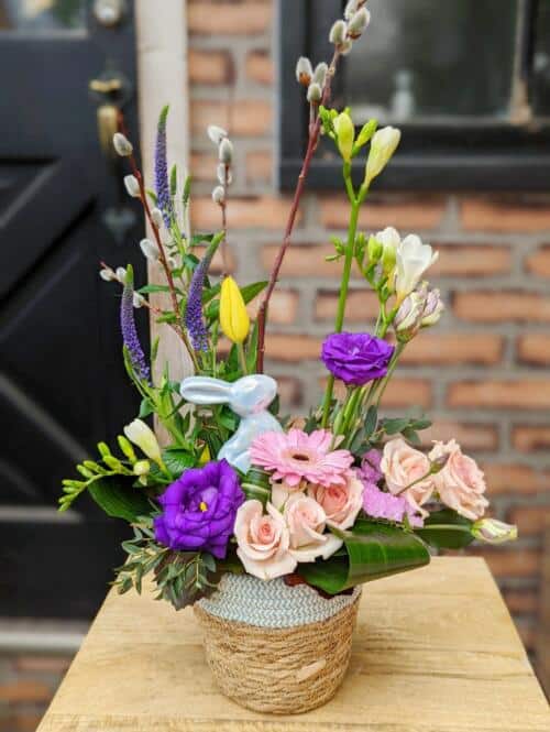 The Watering Can | A purple, white, and yellow European style arrangement with a pale blue ceramic bunny in a light blue basket.