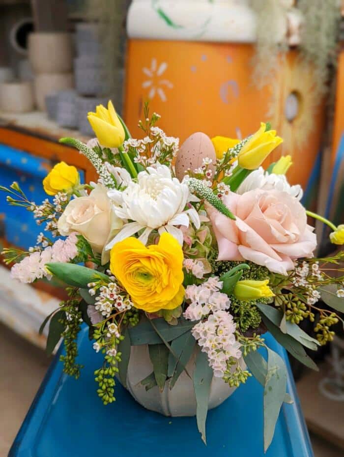 The Watering Can | A soft blush, yellow, and white, European style floral arrangement overflowing from a round beige ceramic container.