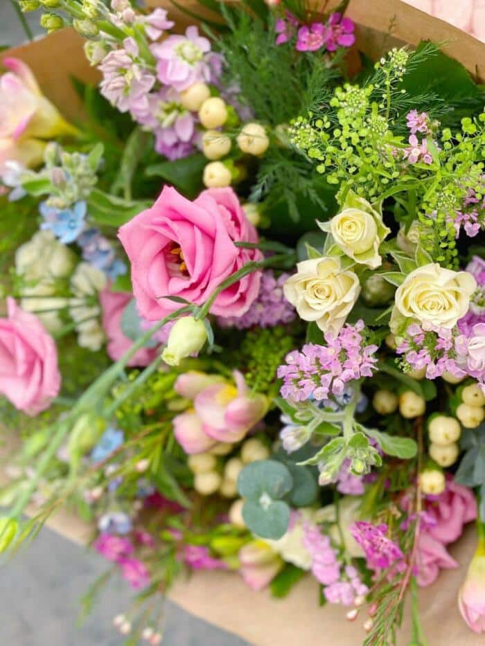 The Watering Can | Close up of the freesia, spray roses, statice, hypericum, and eucalyptus in a pink garden bouquet.