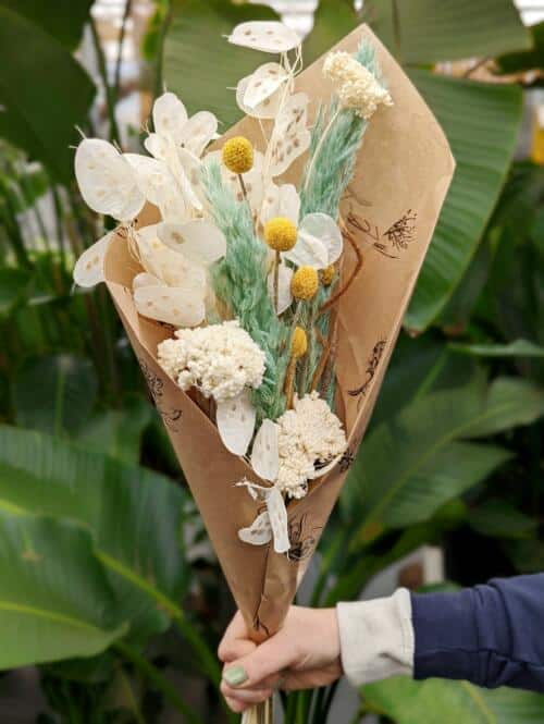 The Watering Can | A bundle of dried flowers in white, seafoam green, and a op of yellow wrapped in brown paper.