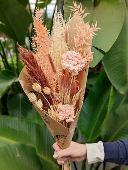 The Watering Can | A bundle of dried flowers in peach, terracotta, and blush tones wrapped in brown paper.