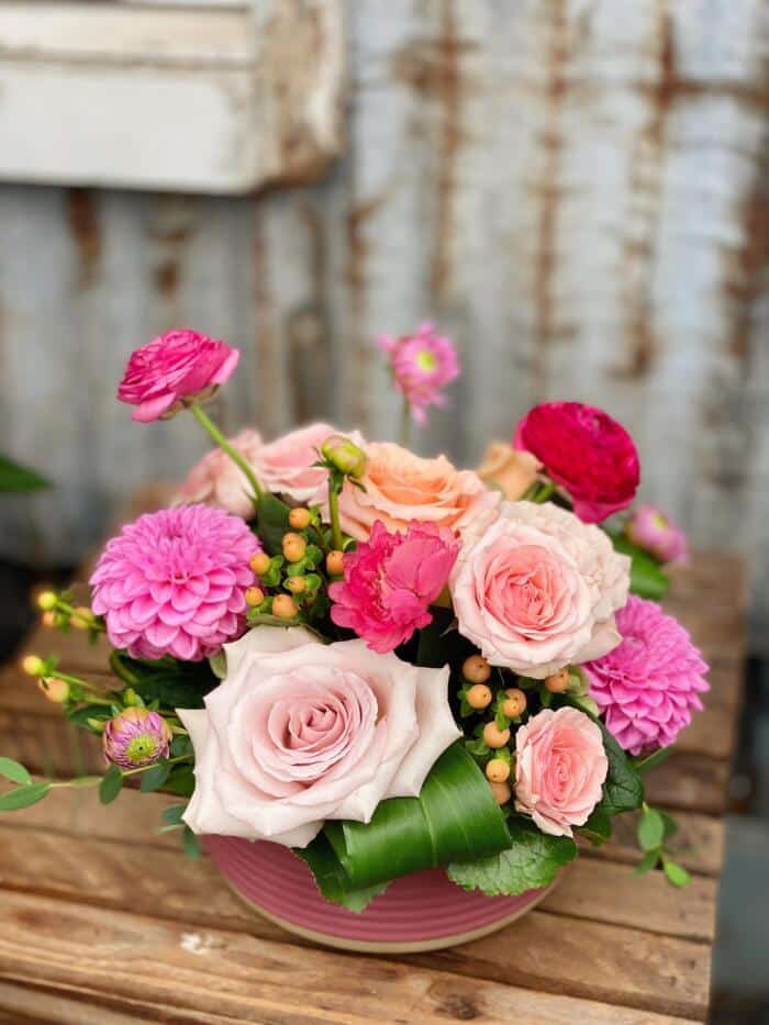 The Watering Can | A low European style floral arrangement made with pink roses, ranunculus, and dahlias.